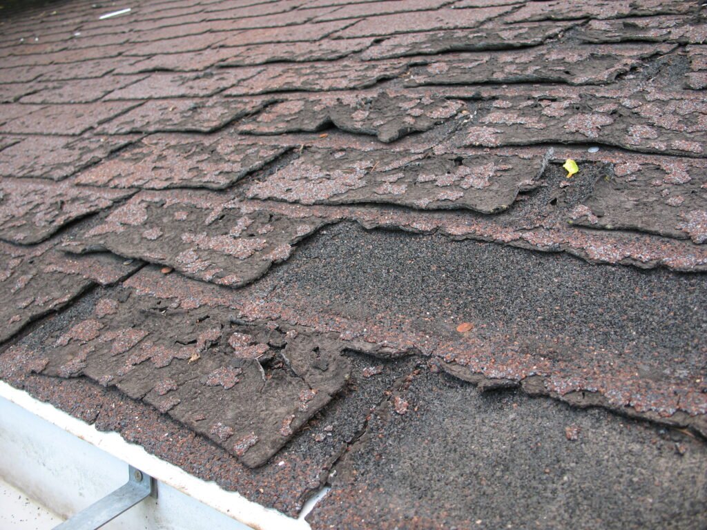 Weathered asphalt shingles with curling edges and exposed fasteners